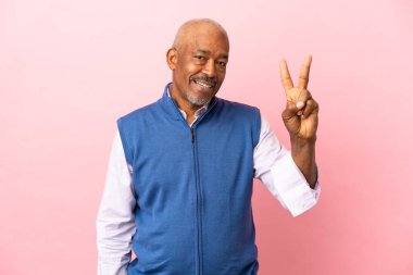 Kübalı son sınıf öğrencisi pembe arka planda izole edilmiş gülümsüyor ve zafer işareti gösteriyor