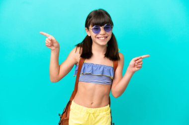 Küçük beyaz bir çocuk kumsala gidiyor. Mavi arka planda izole edilmiş. Parmak uçlarını işaret ediyor ve mutlu.