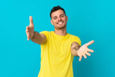 Mavi arka planda soyutlanmış beyaz, yakışıklı genç bir adam sunar ve davet eder.