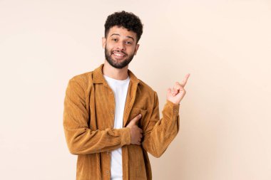 Bej arka planda izole edilmiş genç Faslı adam mutlu ve dik duruyor.