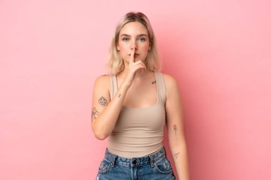 Pembe arka planda izole edilmiş beyaz bir kadın sessiz bir jest işareti gösteriyor. Parmağını ağzına sokuyor.