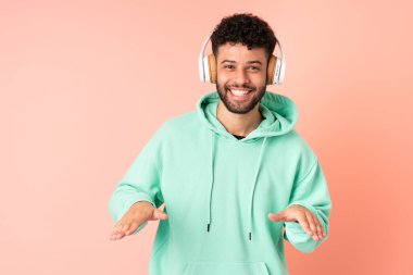 Genç Faslı adam pembe arka planda izole edilmiş müzik ve dans dinliyor.