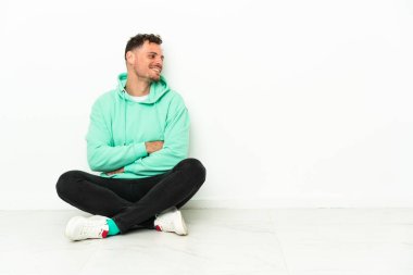 Genç, yakışıklı, beyaz bir adam yerde oturuyor.