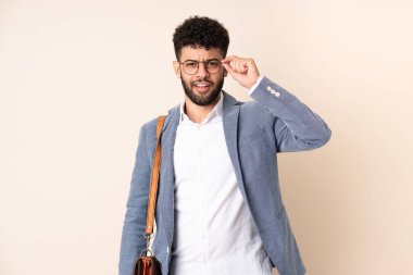 Genç Faslı iş adamı bej arka planda gözlüklü ve şaşırmış bir şekilde izole edilmiş.