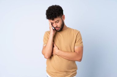 Faslı genç bir adam mavi arka planda başağrısı ile izole edilmiş.