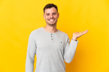 Beyaz, yakışıklı, sarı arka planda izole edilmiş genç bir adam. Avucunun içinde hayali bir fotokopi makinesi tutuyor.