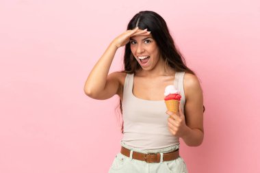 Kornet dondurması olan beyaz bir kadın pembe arka planda izole edilmiş. Yan tarafa bakarken sürpriz jest yapıyor.