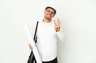 Miğferli ve elinde planları olan genç mimar beyaz arka planda izole edilmiş mutlu ve parmaklarıyla üçe kadar sayıyor.