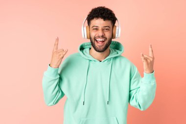 Genç Faslı bir adam pembe arka planda izole edilmiş rock müziği dinliyor ve jest yapıyor.