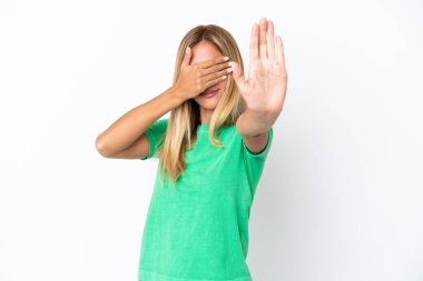 Sarışın Uruguaylı kız beyaz arka planda izole edilmiş. Durma hareketi yapıyor ve yüzünü kapatıyor.