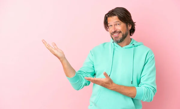 シニアオランダ人男隔離上のピンクの背景伸張手へザ側への招待のために来る — ストック写真