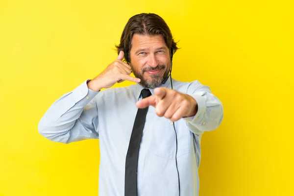 黄色の背景に隔離されたヘッドセットで働くテレマーケティング担当者オランダ人男性電話ジェスチャーを作り 前を指す — ストック写真