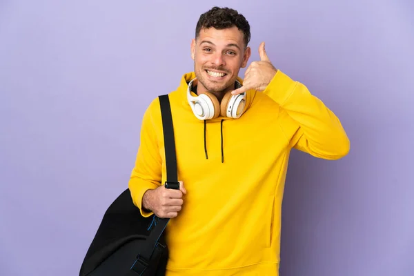 Young sport caucasian man with bag isolated purple background making phone gesture. Call me back sign