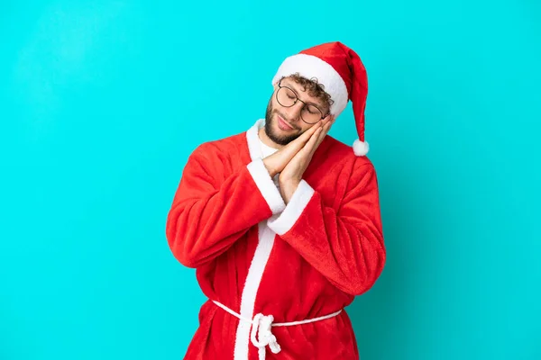 装扮成圣诞老人的年轻人在蓝色背景下孤立无援 带着安稳的表情打瞌睡 — 图库照片