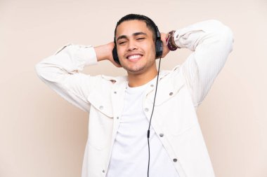 Asyalı yakışıklı adam bej arka planda izole edilmiş müzik dinliyor.