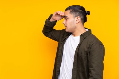 Asyalı yakışıklı adam sarı arka planda izole edilmiş. Parmaklarıyla işaret veriyor.