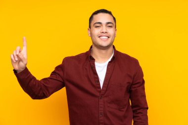 Asyalı yakışıklı adam sarı arka planda izole edilmiş bir şekilde parmağını kaldırarak çözümü bulmaya çalışıyor.