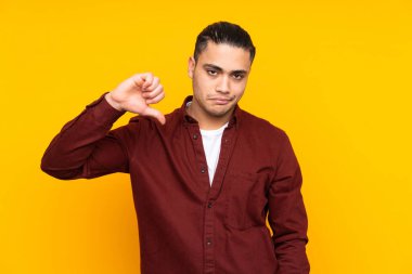 Sarı arka planda izole edilmiş Asyalı yakışıklı bir adam bir ürün sunmak için kenarı işaret ediyor.