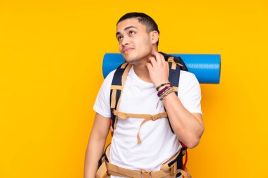 Sarı arka plana izole edilmiş büyük sırt çantalı Asyalı genç bir adam bir fikir düşünüyor.