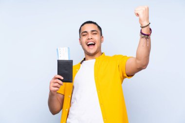 Asyalı yakışıklı adam mavi arka planda izole edilmiş. Pasaportu ve uçak biletleri ile tatilde mutlu.
