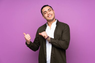 Asyalı yakışıklı adam mavi arka planda izole edilmiş bir şekilde bir ürün sunmak için kenarı işaret ediyor.