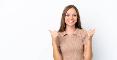 Genç Litvanyalı bir kadın beyaz arka planda izole edilmiş, başparmakları havada ve gülümsüyor.