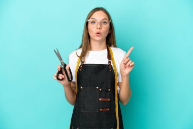 Genç Litvanyalı terzi kadın mavi arka planda izole edilmiş. Çözümü bulmak için parmağını kaldırıyor.