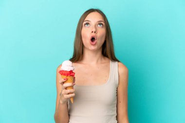 Kornet dondurmalı genç Litvanyalı kadın mavi arka planda izole edilmiş yukarı bakıyor ve şaşırmış bir ifadeyle