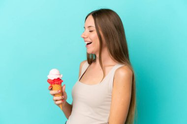 Kornet dondurması olan Litvanyalı genç bir kadın mavi arka planda izole edilmiş. Yan pozisyonda gülüyor.
