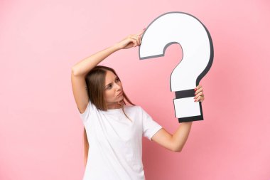 Genç Litvanyalı bir kadın pembe arka planda izole edilmiş. Elinde soru işareti simgesi var.