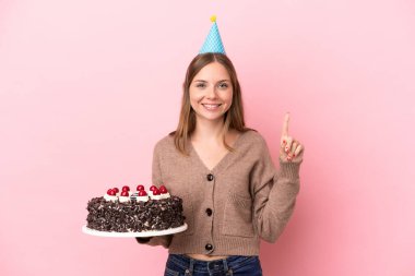 Elinde doğum günü pastası tutan genç Litvanyalı kadın pembe arka planda izole edilmiş harika bir fikre işaret ediyor.