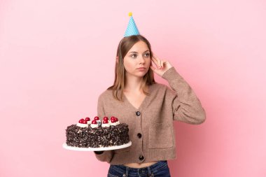 Elinde doğum günü pastası tutan Litvanyalı genç bir kadın pembe arka planda izole edilmiş şüpheleri ve düşünceleri var.