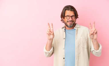 Pembe arka planda izole edilmiş kıdemli Hollandalı iki elle zafer işareti gösteriyor.