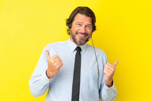 テレマーケティング担当者オランダ人男作業ヘッドセットで隔離された黄色の背景に親指アップジェスチャーと笑顔 — ストック写真