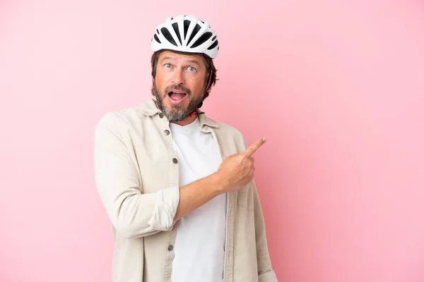 シニアオランダ人男とともにバイクヘルメット隔離上のピンクの背景驚きと指摘側 — ストック写真