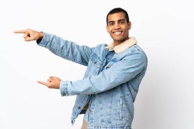 İzole edilmiş beyaz arka planda yaşayan Afro-Amerikalı bir adam parmağını yana uzatıp bir ürün sunuyor.