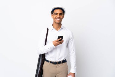 Miğferli Afrikalı Amerikalı mimar ve izole edilmiş beyaz arkaplan üzerinde planları olan _ cep telefonuyla bir mesaj gönderiyor