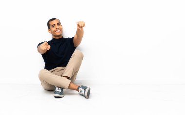 Yerde oturan Afrikalı Amerikalı adam gülümserken seni işaret ediyor.