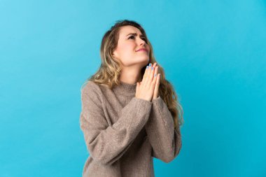 Mavi arka planda izole edilmiş genç Brezilyalı kadın avuç içlerini bir arada tutuyor. İnsan bir şey ister.