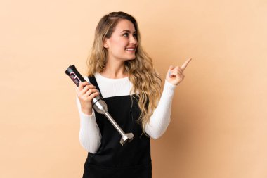 Bej arka planda izole edilmiş el blenderi kullanan genç Brezilyalı kadın harika bir fikre işaret ediyor.