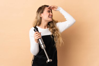 Bej arka planda izole edilmiş el blenderi kullanan genç Brezilyalı kadın çok gülümsüyor.