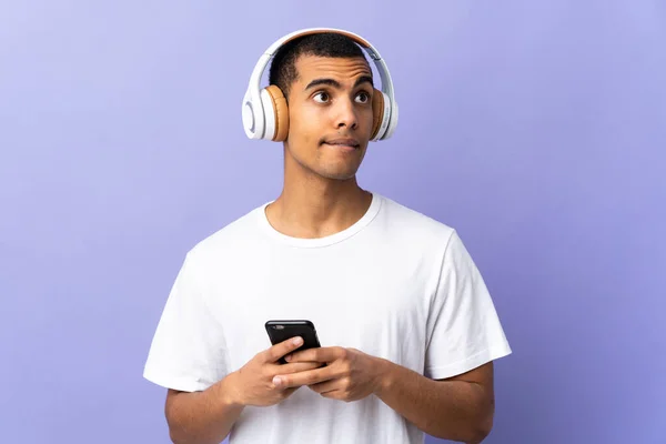 非洲裔美国人越过孤立的紫色背景 一边用手机一边听音乐一边思考 — 图库照片
