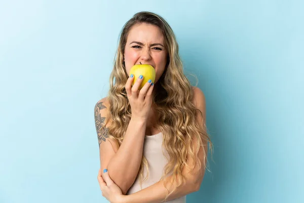 Joven Brasileña Aislada Sobre Fondo Azul Comiendo Una Manzana — Foto de Stock