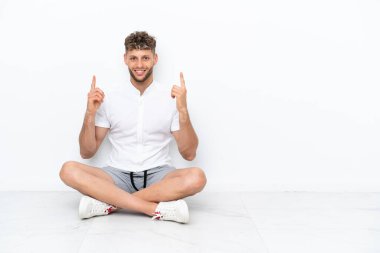 Genç sarışın adam beyaz arka planda izole bir şekilde yerde oturuyor. Harika bir fikir.