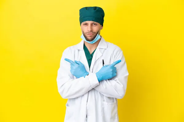 Χειρούργος Ξανθός Άντρας Πράσινη Στολή Απομονωμένος Κίτρινο Φόντο Που Δείχνει — Φωτογραφία Αρχείου