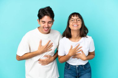 Mavi arka planda soyutlanmış genç melez bir çift ellerini göğsüne koyup gülümsüyor.