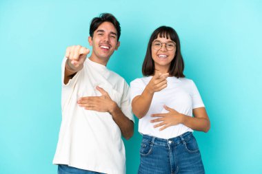 Mavi arka planda soyutlanmış genç melez bir çift birini işaret ediyor ve çok gülüyor.