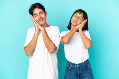 Mavi arka planda soyutlanmış genç melez bir çift, uyku jesti yapıyor.