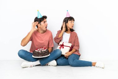 Genç melez çift, beyaz arka planda izole bir şekilde yerde oturmuş bir şeyler dinliyorlardı.