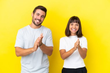 Sarı arka planda izole edilmiş genç bir çift, bir konferanstan sonra alkışlıyorlar.